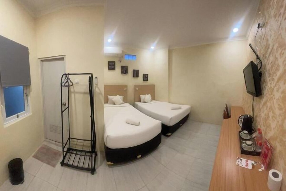 A hotel room with two beds, a shower, a sink, and a TV.