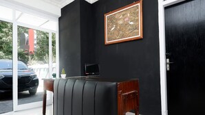 Een kamer met een zwarte leren bank, een houten bijzettafeltje, een kunstwerk in een lijst aan de muur en een deur.