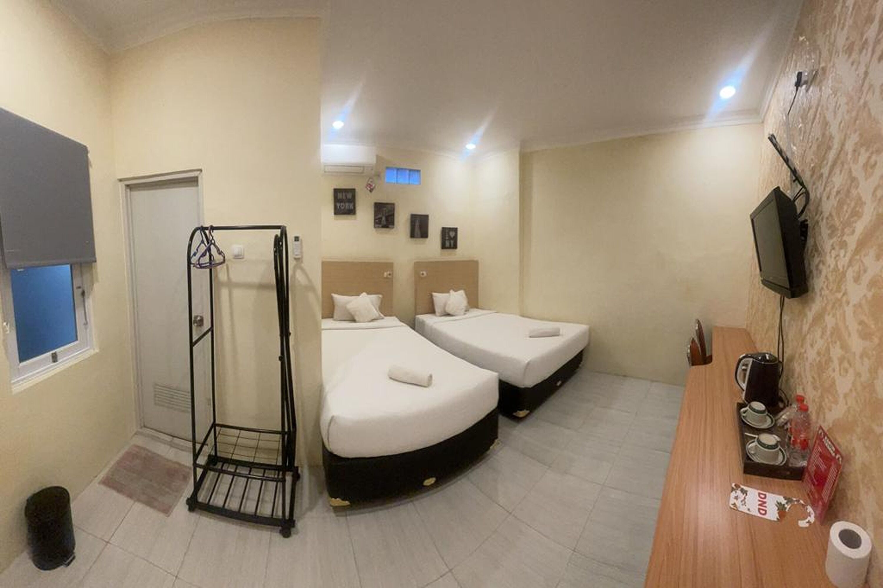 A hotel room with two beds, a desk with a coffee machine, a TV, and a shower area.