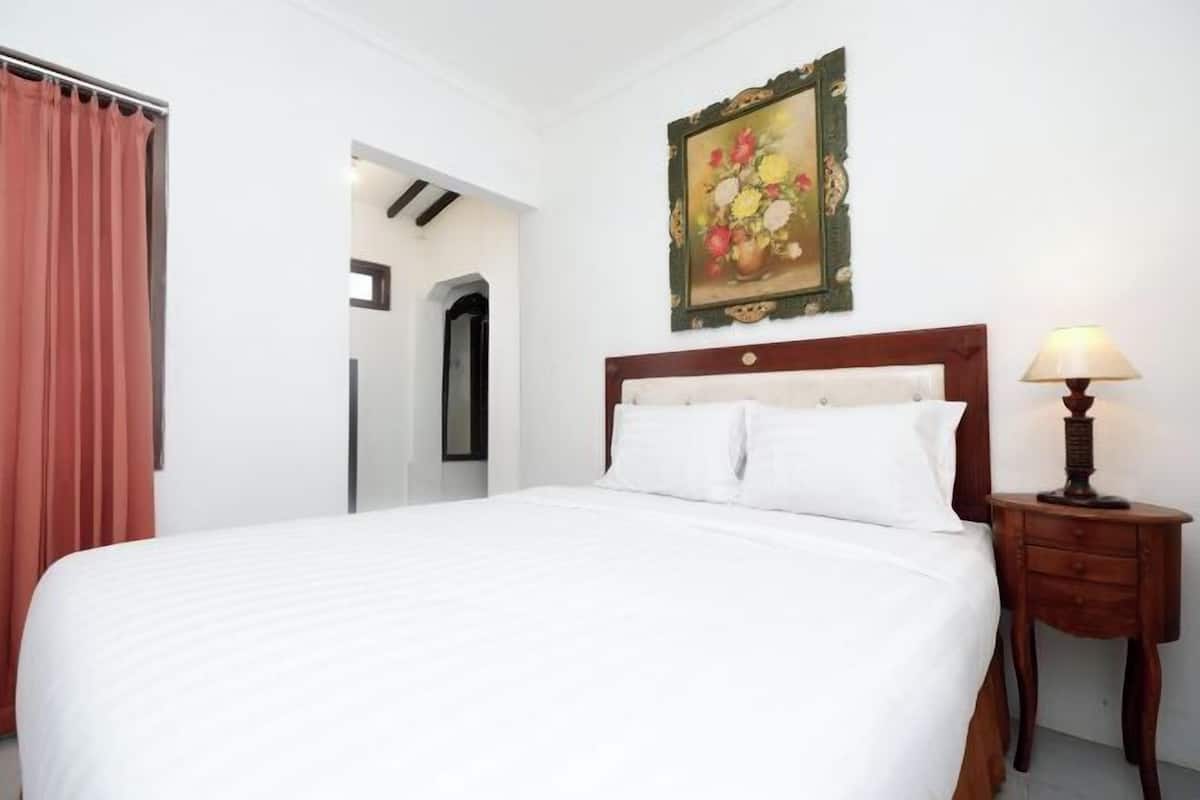 A hotel room with a large bed, a wooden headboard, a nightstand with a lamp, and a painting on the wall.