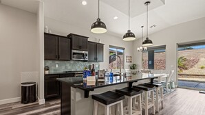Una cocina moderna con armarios oscuros, una isla central con taburetes y luces colgantes.