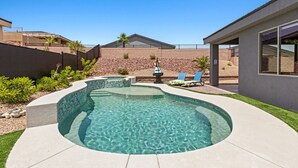Un patio trasero con piscina, un porche con dos sillones de descanso y un pequeño hogar para fuego.