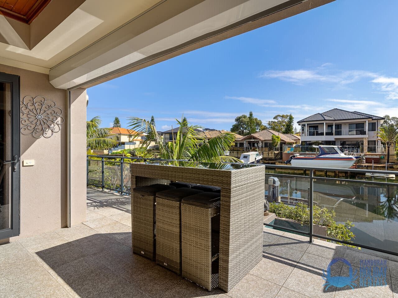 A balcony with wicker furniture, a decorative metal piece, and a view of a marina with boats and houses.