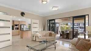 A modern living room with a glass coffee table, a sofa, and a dining area with outdoor seating.