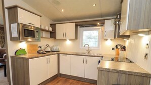 A compact kitchen with a microwave, toaster, sink, and wooden flooring. - 41, Grandma's Cottage (Carnforth)