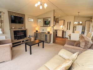 A living room with a TV, sofa, coffee table, and a kitchen area in the background.