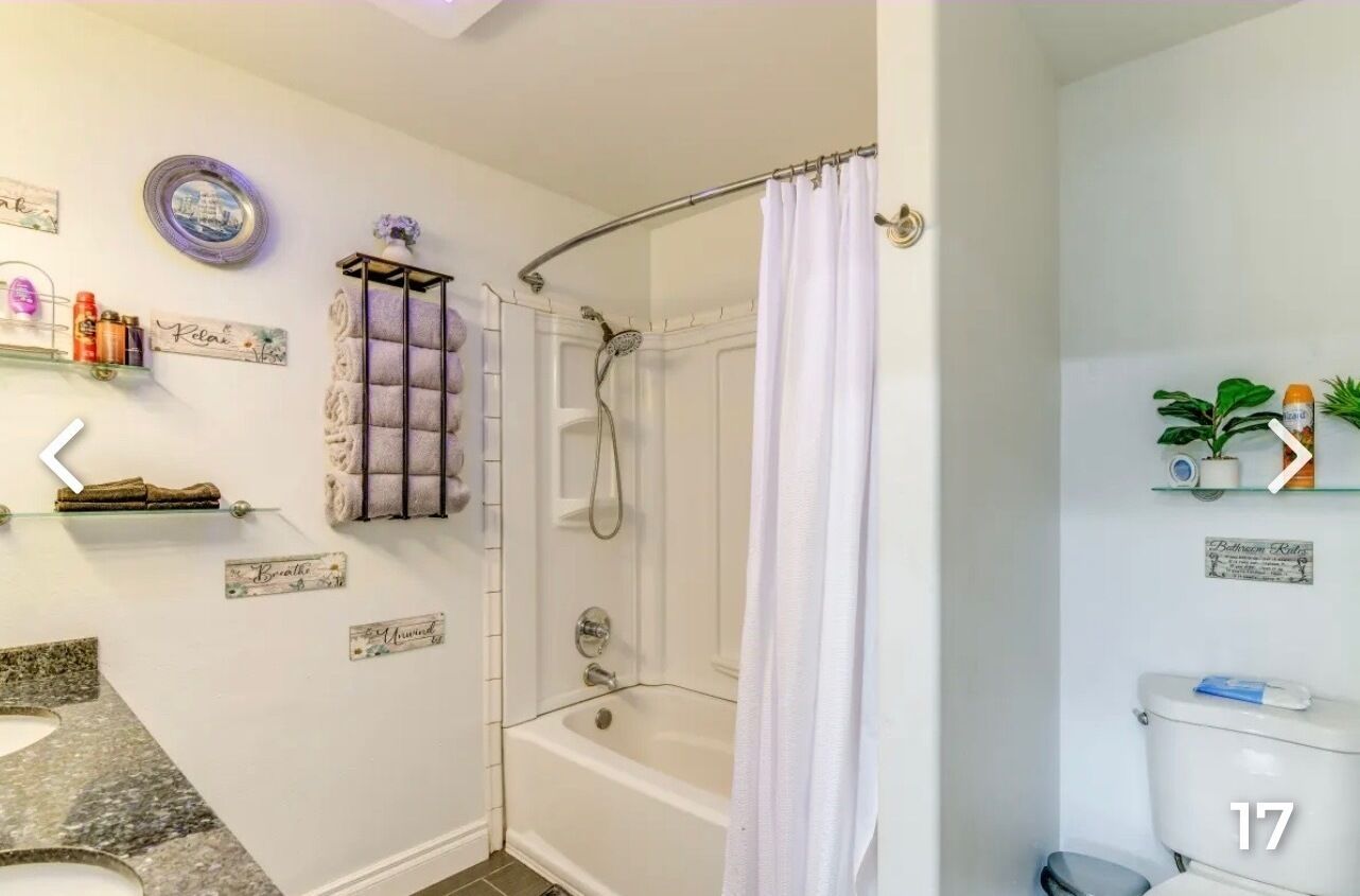 Een badkamer met een bad, douche, toilet en een wastafelmeubel. Er liggen decoratieve handdoeken en een klein plankje met toiletartikelen.