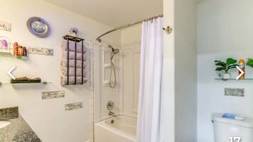 Een badkamer met een bad, douche, toilet en een wastafelmeubel. Er liggen decoratieve handdoeken en een klein plankje met toiletartikelen.