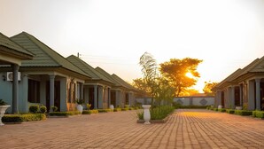 A row of traditional-style buildings with a paved walkway in the center. - Golden Hills Lodge (Kafue)