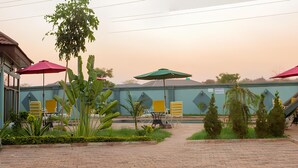 A courtyard with brick flooring, outdoor seating, and umbrellas. - Golden Hills Lodge (Kafue)