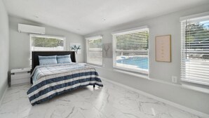 A bedroom with a bed, nightstands, a marble floor, and large windows with blinds.