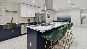 A modern kitchen with a central island, stainless steel appliances, and a high ceiling.