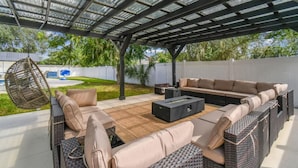 An outdoor patio with a covered seating area, including a sofa and a hanging chair.