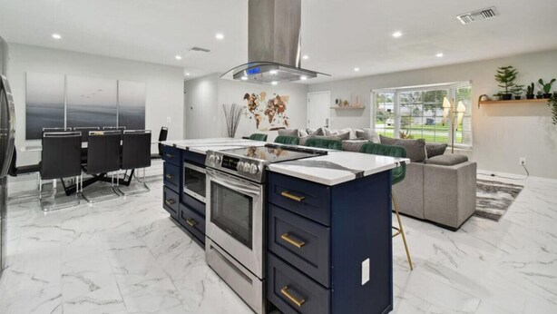 A modern kitchen with a central island, built-in ovens, and a dining area with chairs.