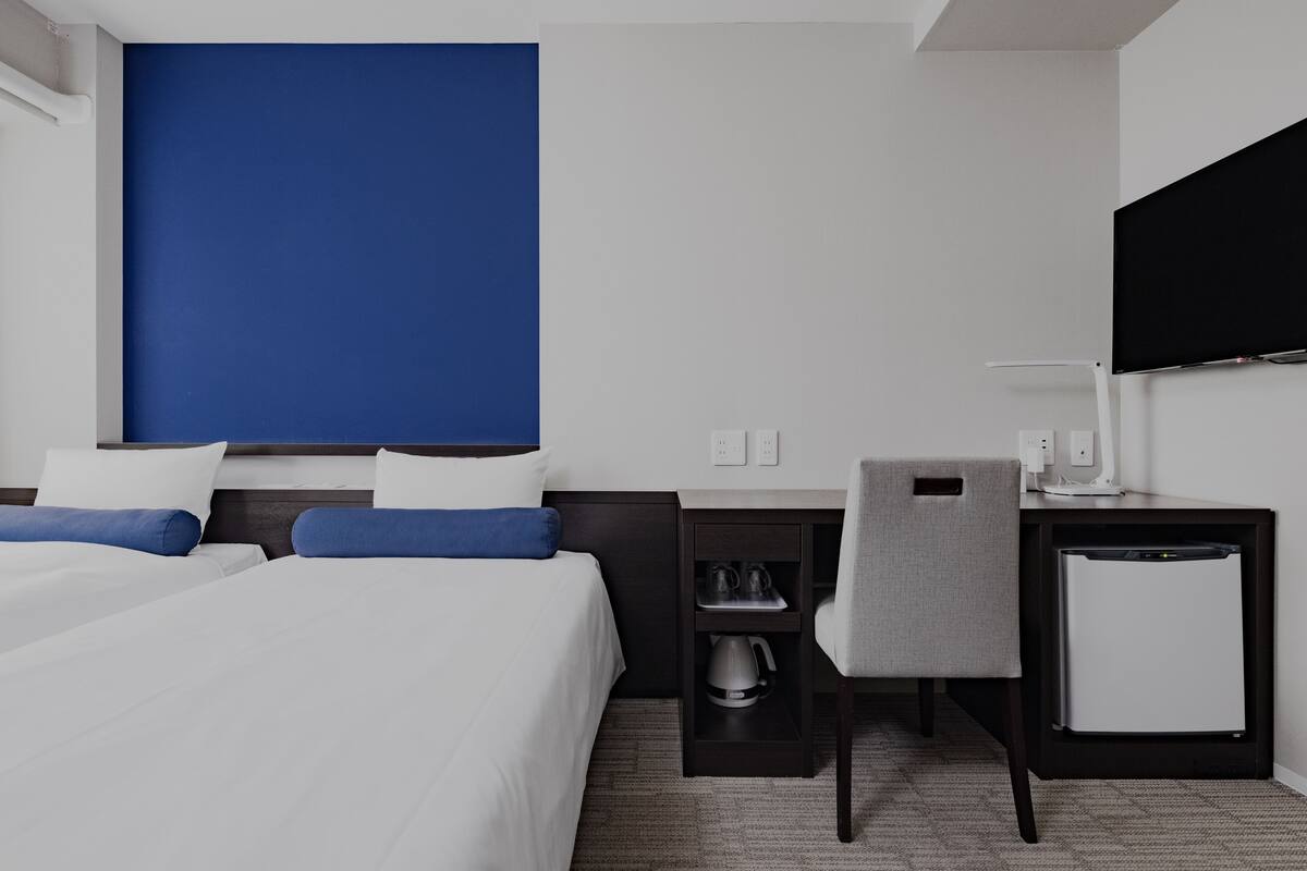 Ein Hotelzimmer mit zwei Betten, einem Schreibtisch mit Stuhl, einem Fernseher und einer Minibar.