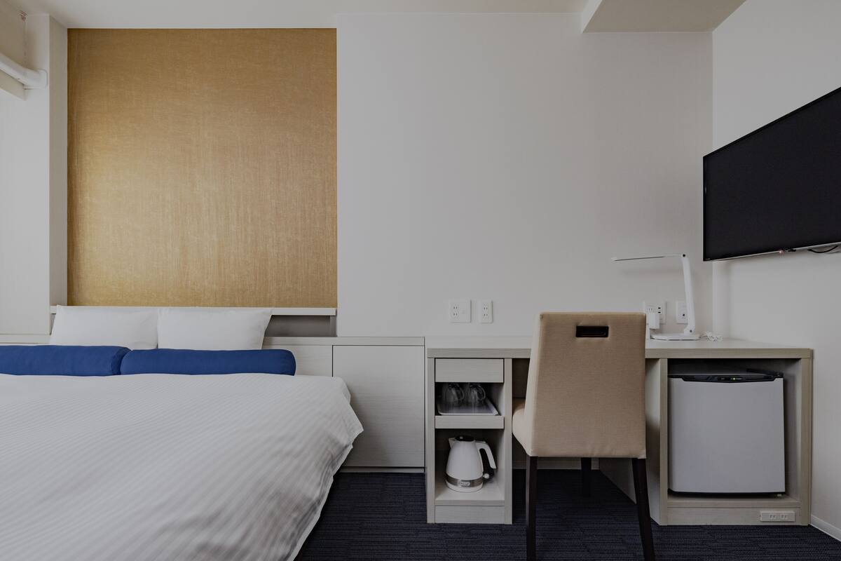 Ein Hotelzimmer mit einem Bett, einem Schreibtisch mit Stuhl, einem Fernseher und einer Kaffeemaschine.