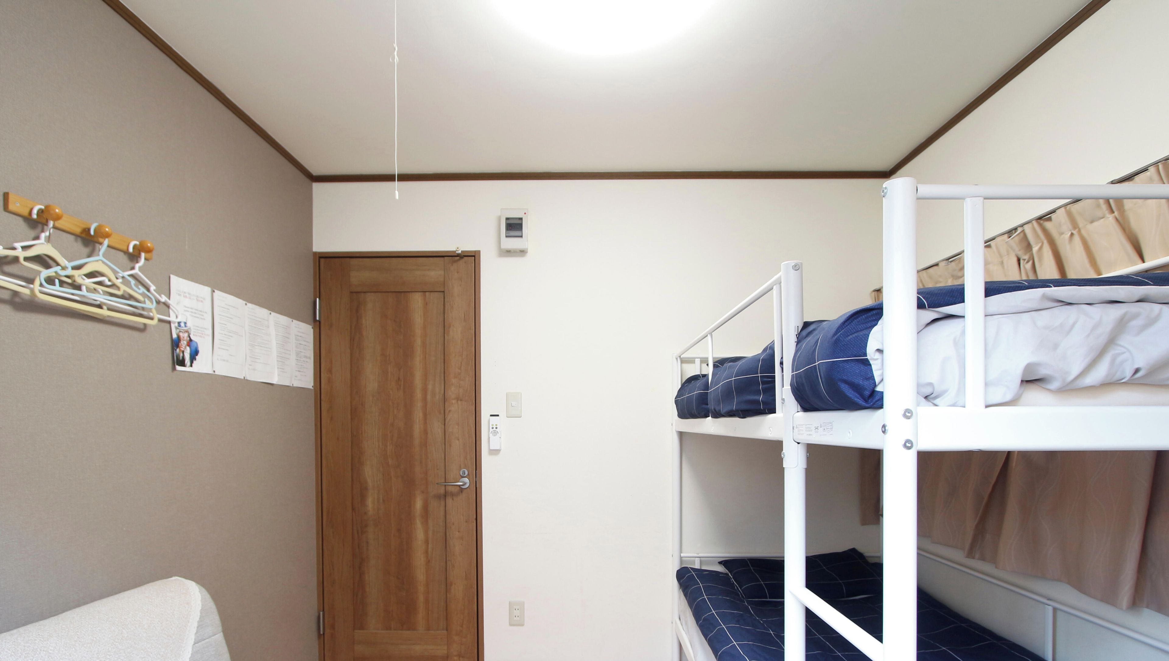 A dormitory room with bunk beds, a wooden door, and a coat rack with hangers.