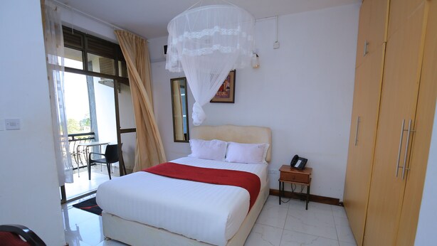 Un dormitorio con cama, mesita de noche, armario, ventana con cortinas y balcón.