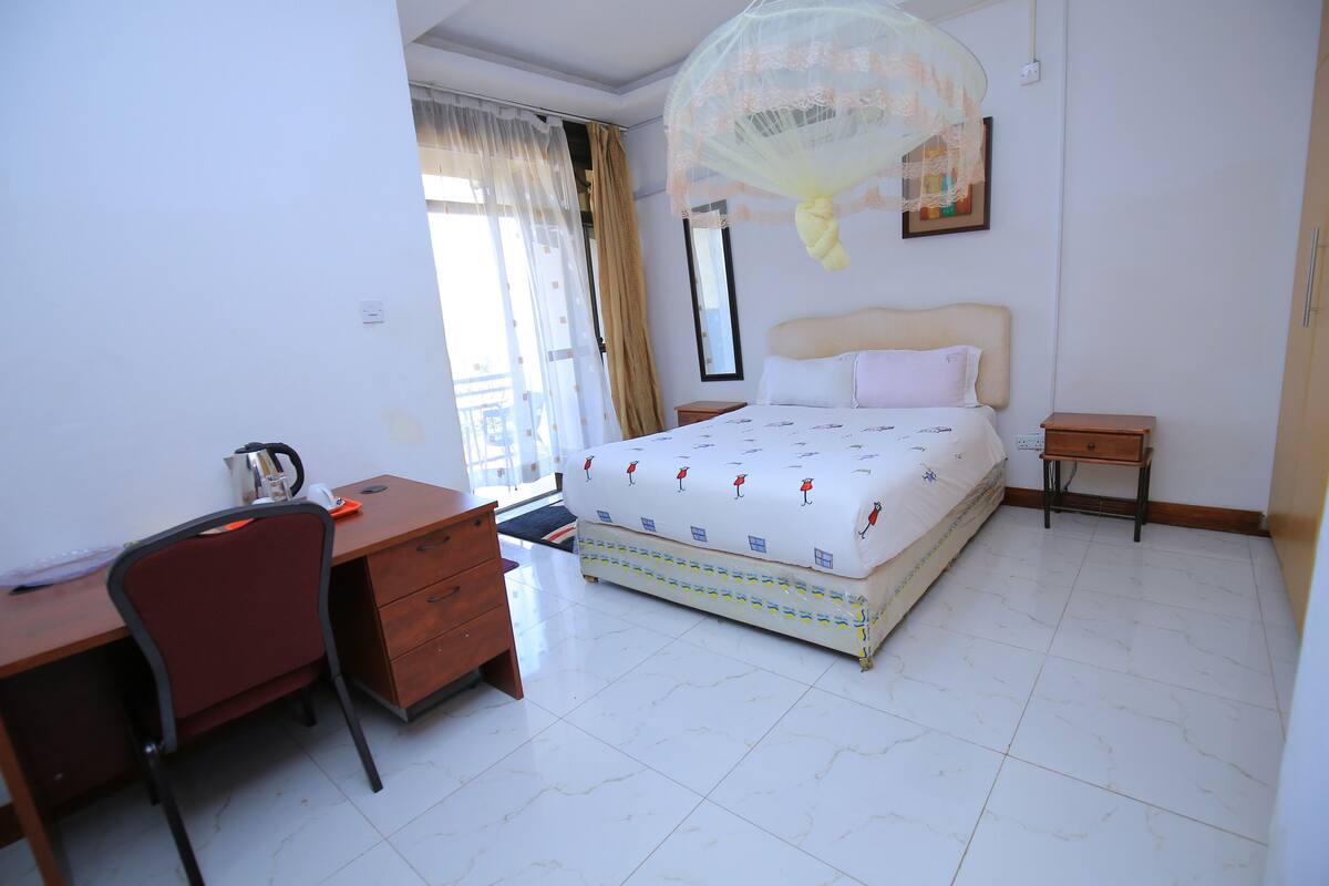 A bedroom with a bed, a desk, a chair, and a bedside table.
