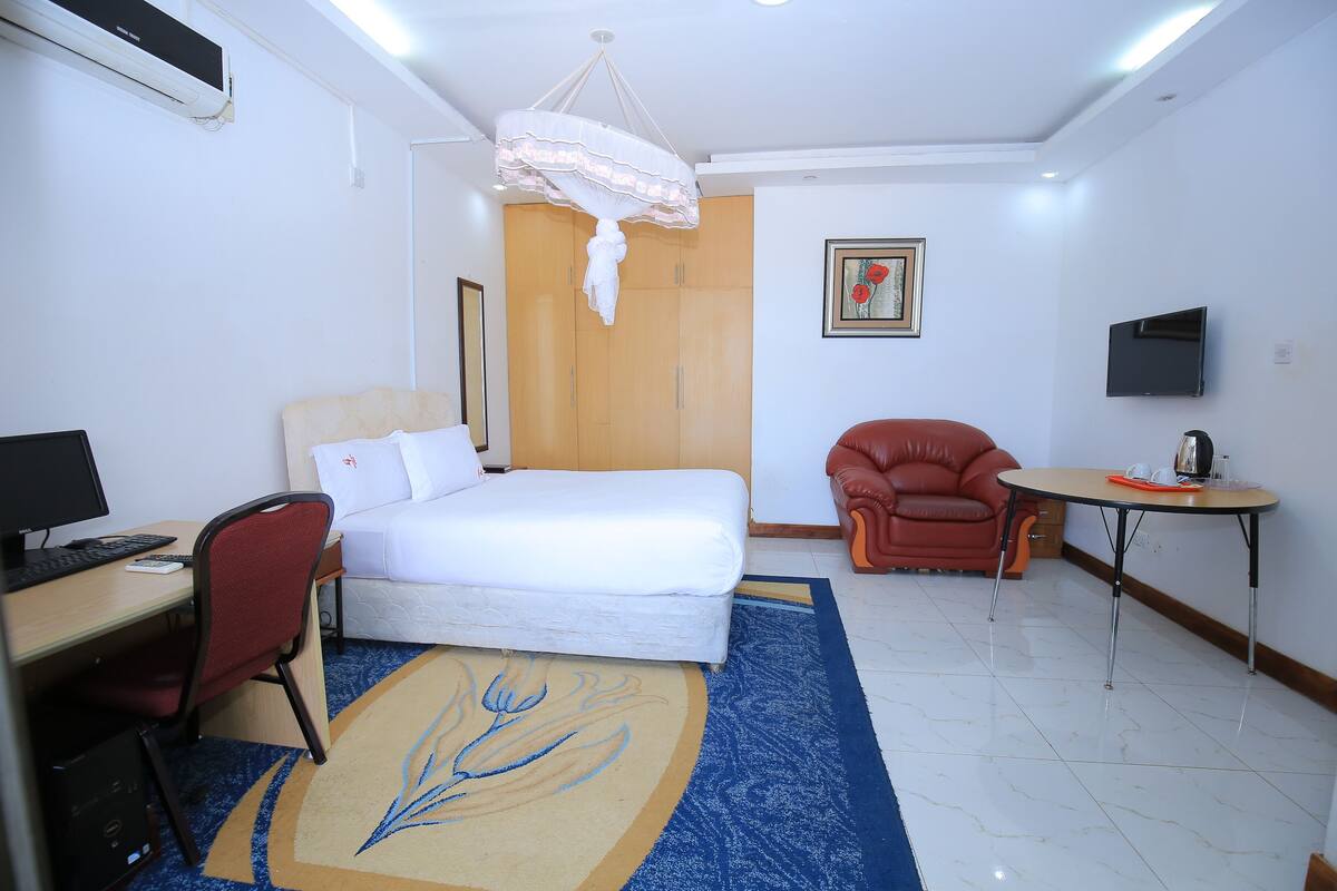 A hotel room with a bed, desk, chair, TV, and a small table.