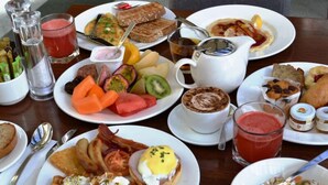 Un bufé de desayuno con diversos platos, entre ellos huevos, tocino, tostadas, frutas y bebidas.
