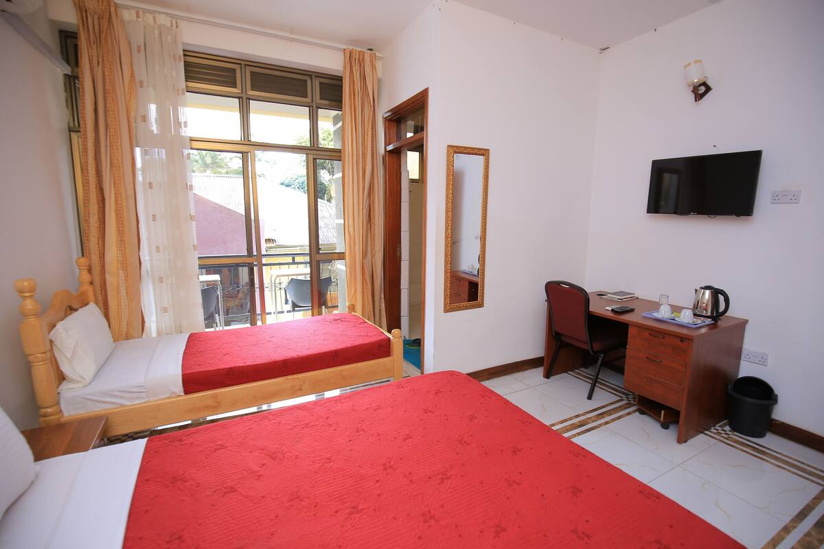 A room with two single beds, a desk with a chair, a television, and a window with curtains.