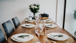 A dining table set with white plates, gold cutlery, and clear glasses, surrounded by chairs. - Villa Melita - Canggu (Canggu)