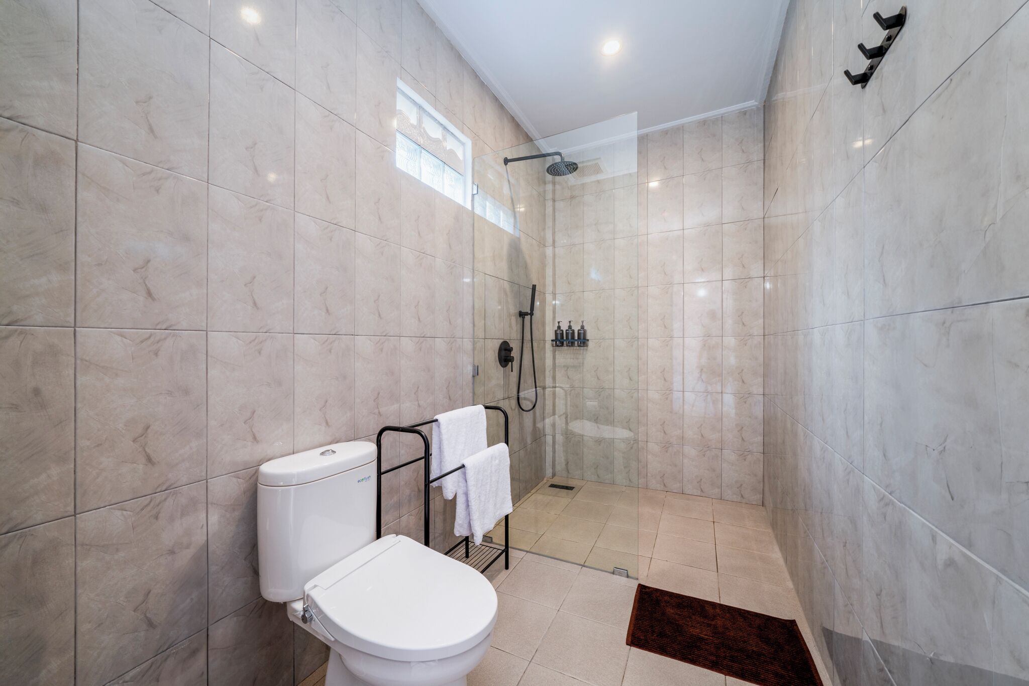 A modern bathroom with a toilet, a glass-enclosed shower, and a towel rack.