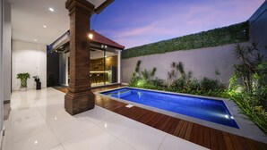 A modern outdoor pool area with a wooden deck, a brick pillar, and a glass-enclosed patio. - Villa Melita - Canggu (Canggu)