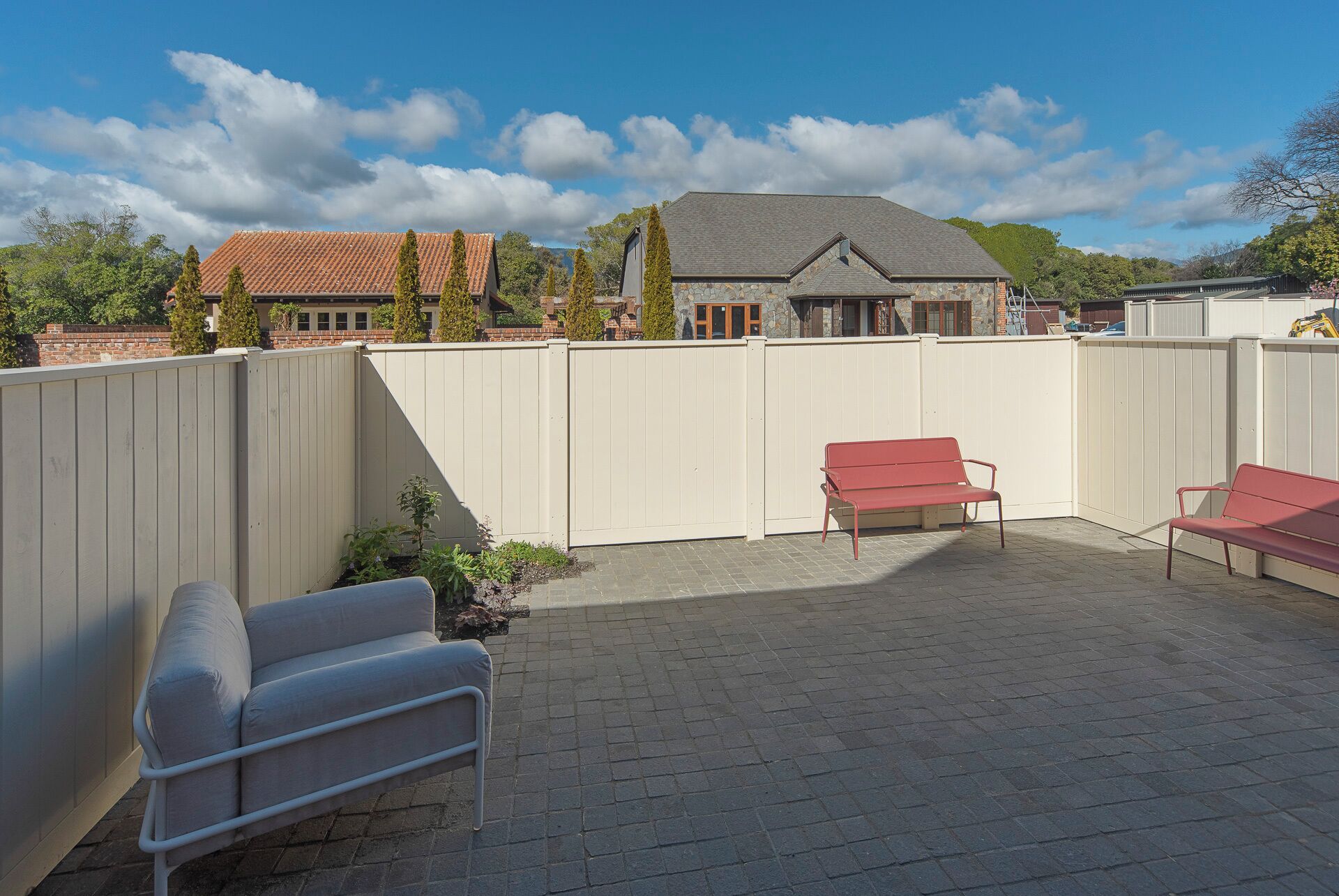 A backyard patio with two red chairs, a white sofa, and a stone wall.