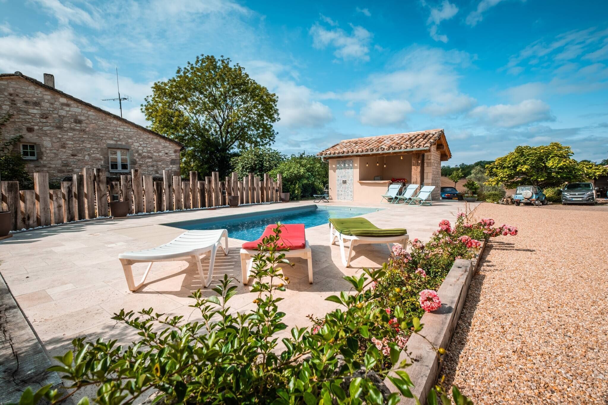 Zona de piscina con sillones, un edificio pequeño y una casa de piedra.