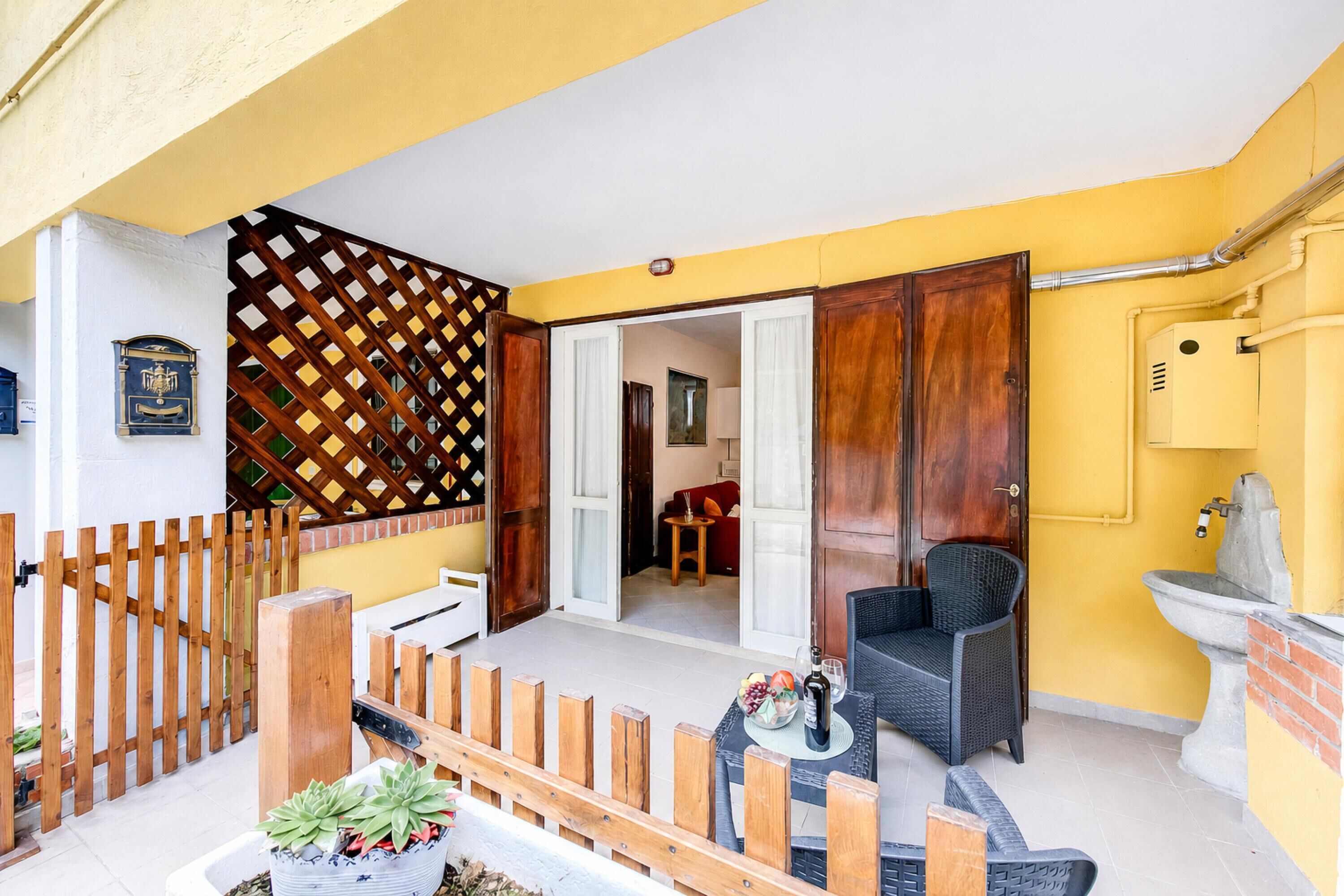 Un'area patio con recinzione in legno, un tavolo da pranzo con sedie, una pianta in vaso e vista sull'interno.