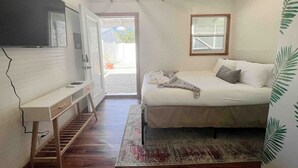 Un dormitorio con cama, escritorio, ventana y puerta que da a un espacio exterior.