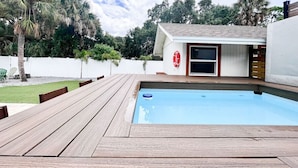 Una piscina con muelle de madera, un puesto de salvavidas y una valla blanca al fondo.