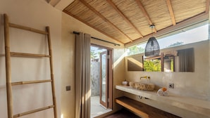 A bathroom with a wooden ladder, a large mirror, and a sink with a stone countertop.