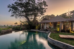 A serene pool area with a thatched-roof structure and lush greenery. - Villa Maison Matisse (Cemagi)