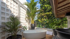 A spa area with a freestanding bathtub, potted plants, and a white wall with a grid pattern.