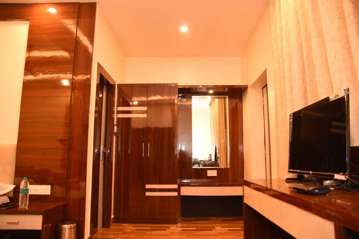 Une chambre d’hôtel avec une armoire en bois, un miroir, une télévision et un petit bureau sur lequel se trouvent une bouteille et une poubelle.