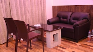 Una habitación con un sofá de cuero marrón oscuro, una mesa de centro de vidrio y dos sillas marrón oscuro.
