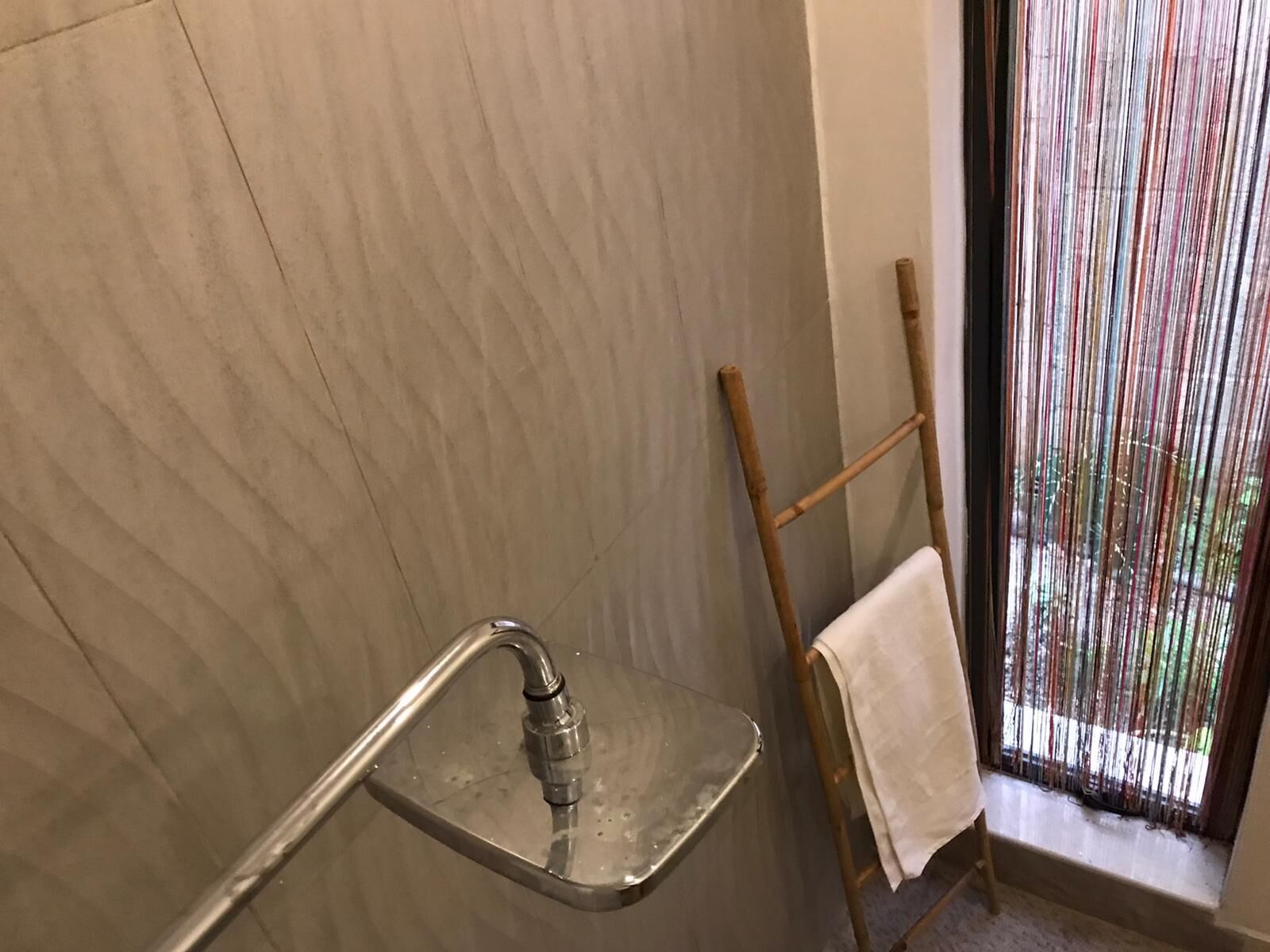 A bathroom with a shower, a wooden ladder, and a window with vertical blinds.