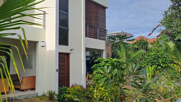 A modern two-story house with a balcony, a front door, and a small porch area with a sofa. - Les Villas Thorel - Hibiscus (La Preneuse)
