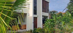 Stylish two-story residence with a clean design, featuring a balcony and lush garden surroundings.