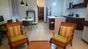 A living room with two armchairs, a coffee table, a dining table with chairs, a kitchen area with a refrigerator, and a small island with a sink. - Les Villas Thorel - Hibiscus (La Preneuse)