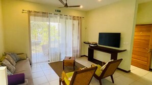 A living room with a sofa, chairs, a TV, and a sliding glass door leading to an outdoor area. - Les Villas Thorel - Hibiscus (La Preneuse)