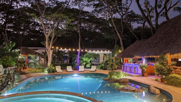 Un área de piscina con sillones de descanso, un bar y una estructura de techo de paja.