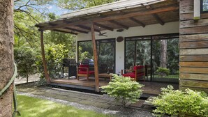 Un patio techado al aire libre con una parrilla, dos sillas rojas y una mesa de madera.