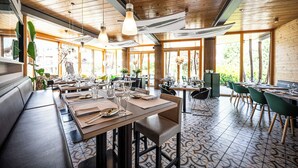 Un restaurant avec des plafonds en bois, de grandes fenêtres et un sol carrelé. Les tables sont dressées avec des assiettes, des verres et des couverts.