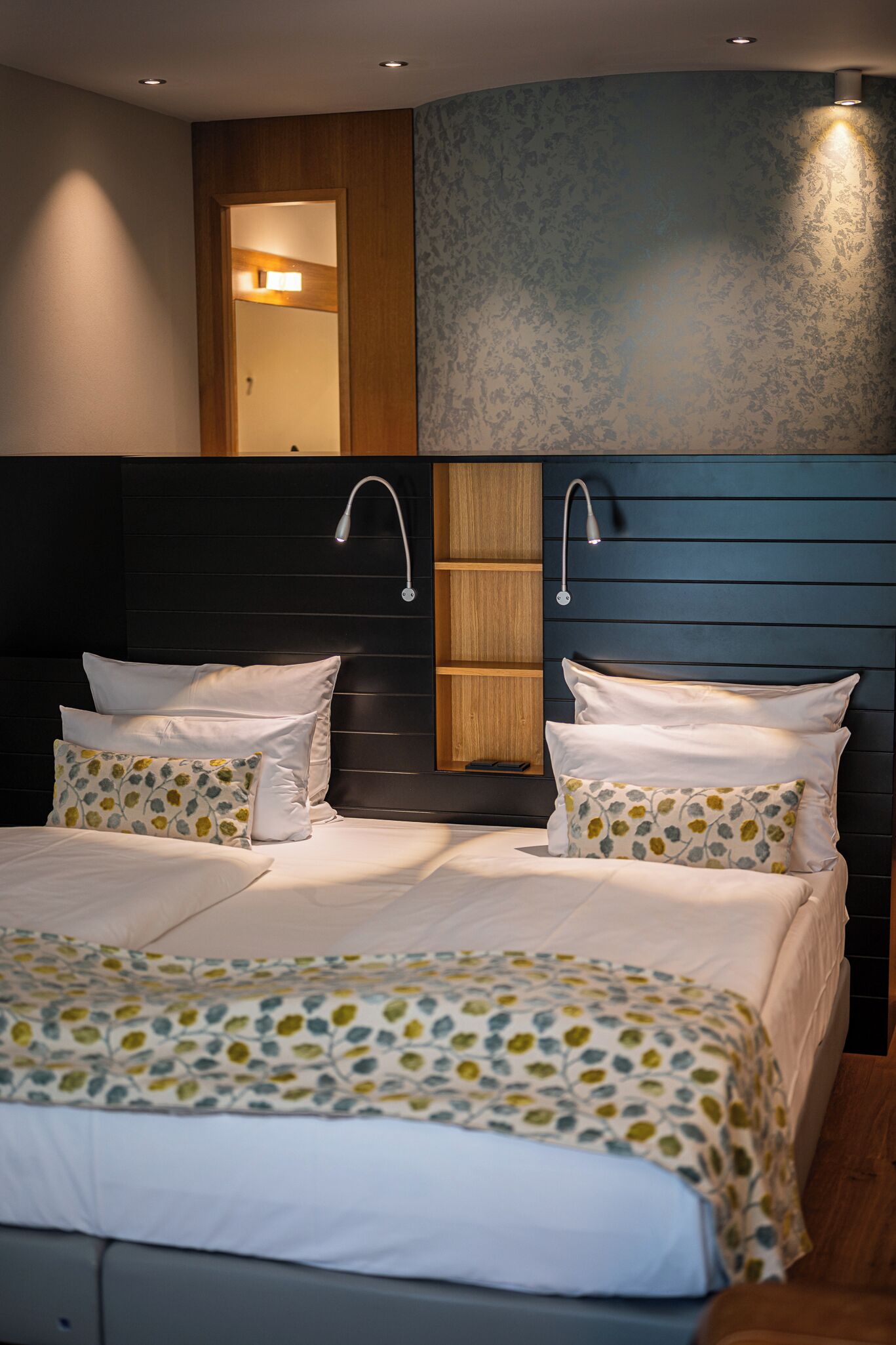 A modern bedroom with a large bed, wooden headboard, and built-in lighting.