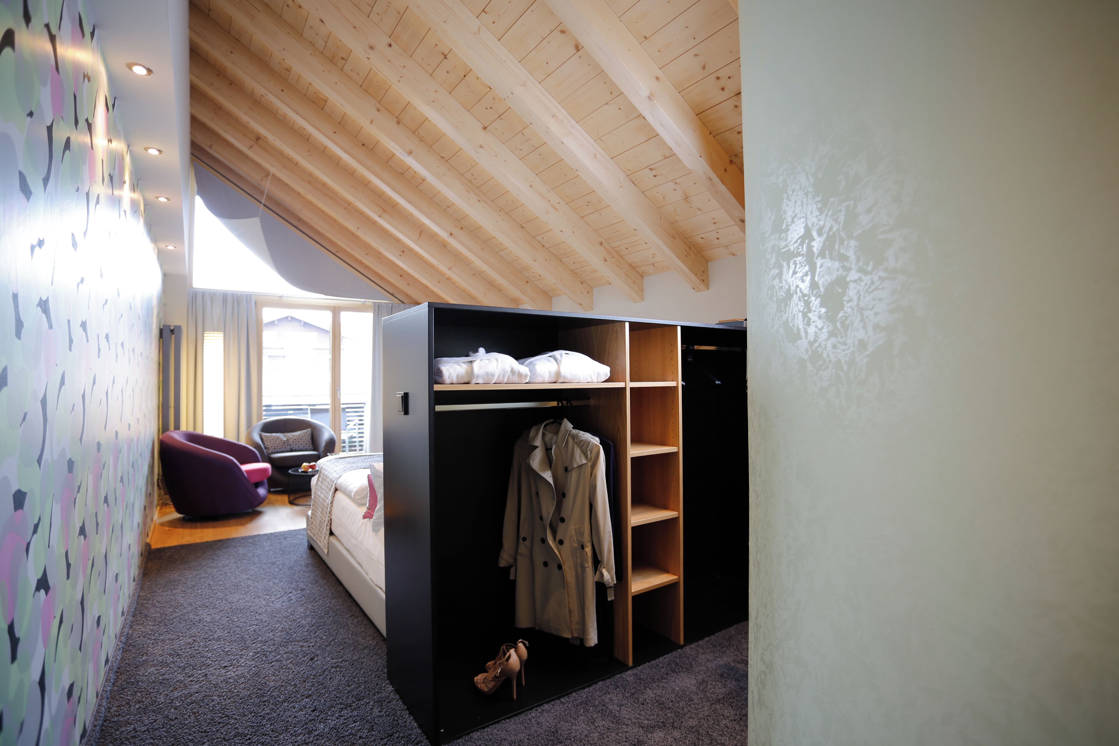 A bedroom with a bed, a chair, a wardrobe, and a coat rack.
