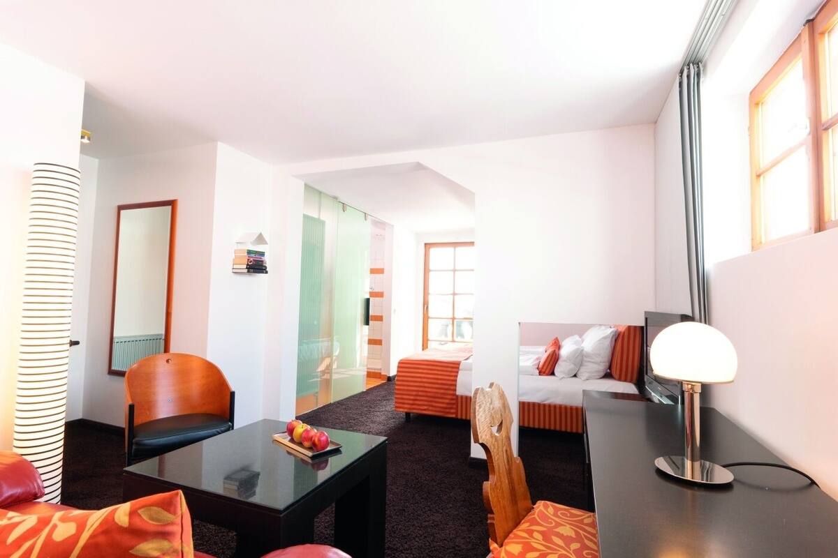 Una habitación de hotel moderna con separador de vidrio, un sofá, una mesa de comedor y una lámpara.